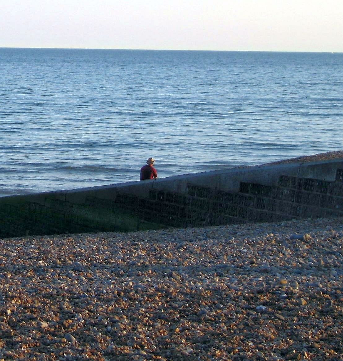 Man in hat sitting on Brighton Beach watching the waves